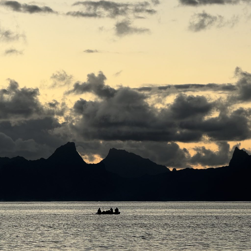 a lonely boat in front of the silhouette of mountains in Moorea, Tahiti, French Polynesia