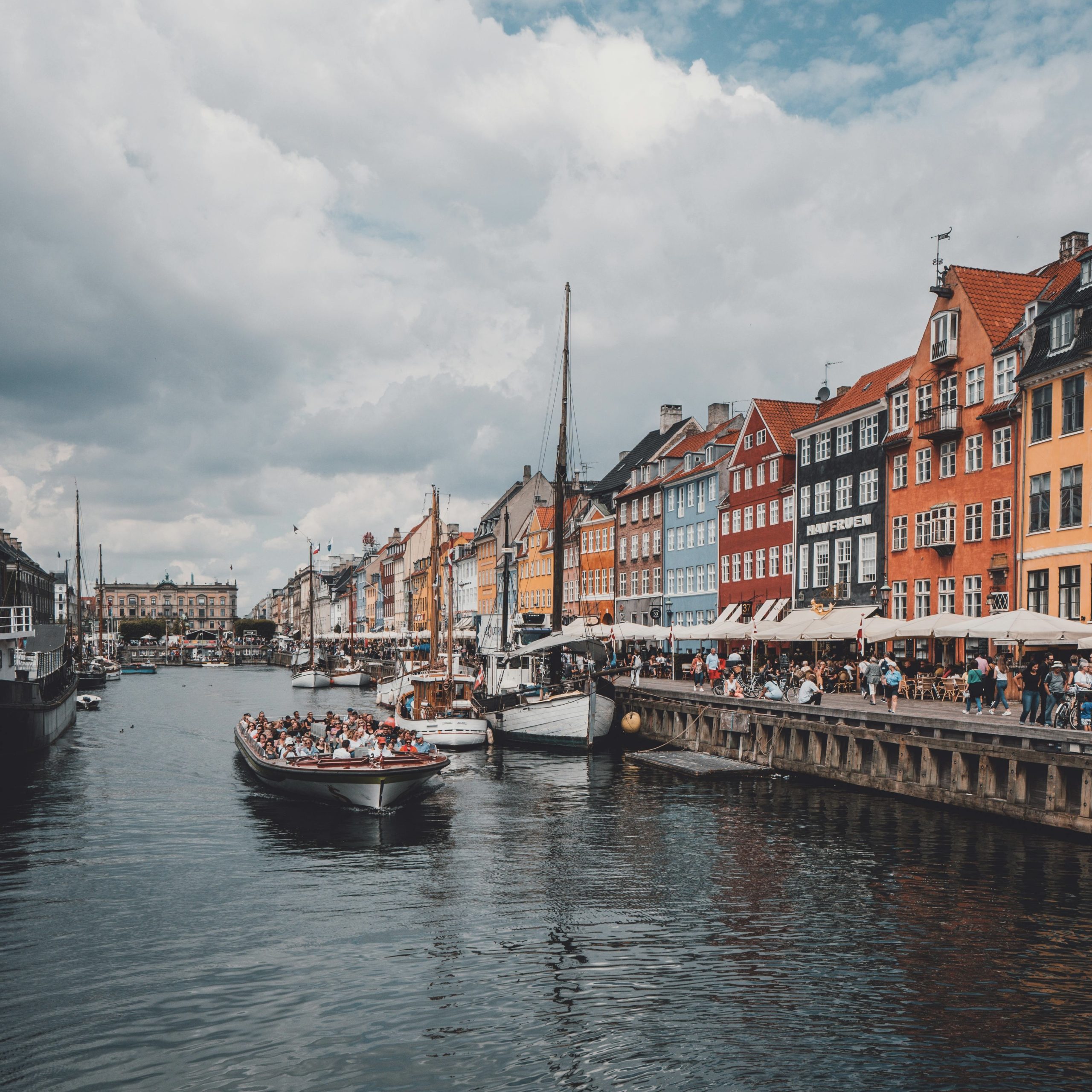 Nyhavn Harbor in Copenhagen, Denmark, featuring colorful historic buildings, lively outdoor cafes, and a boat cruising along the canal, Copenhagen, Denmark