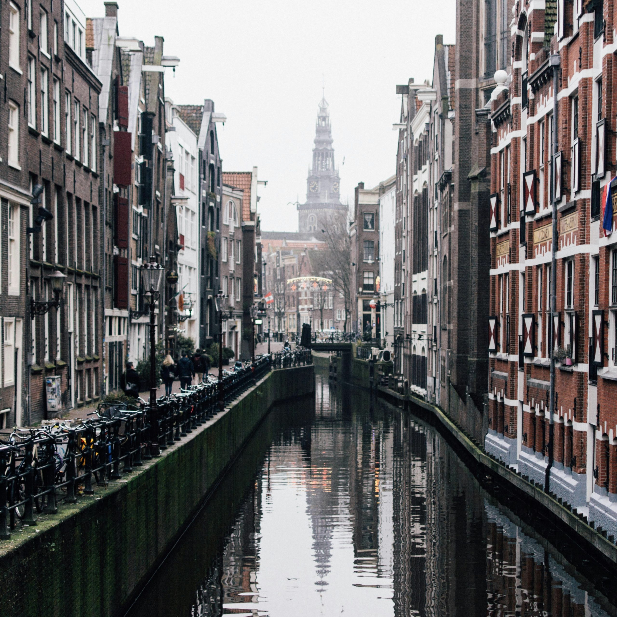 Charming canal view in Amsterdam, Netherlands, lined with historic brick buildings and bicycles, with a church tower visible in the distance, Amsterdam, Netherlands