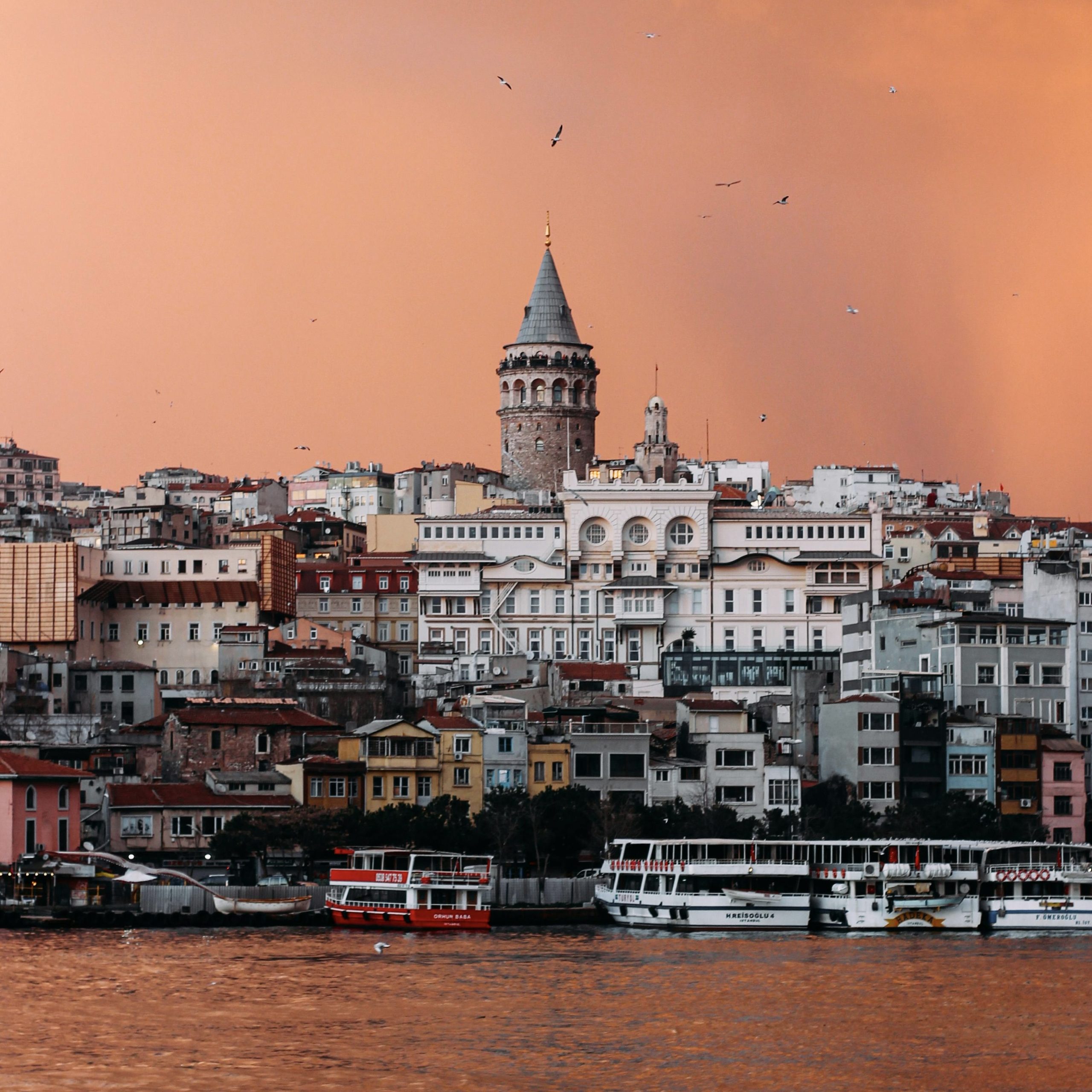 Mesmerizing view of the Galata Tower rising above the colorful buildings of Istanbul, Turkey, with a dramatic orange sunset sky in the background, Istanbul, Turkey
