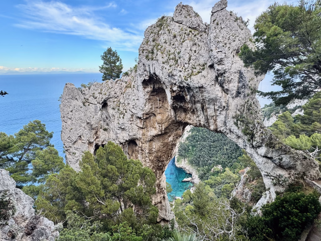 Natural rock arch known as Arco Naturale surrounded by lush greenery with turquoise sea visible through the arch.