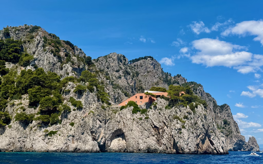 View of Casa Malaparte perched on a rocky cliffside on Capri, with its red exterior standing out against the rugged gray rocks and blue sea.