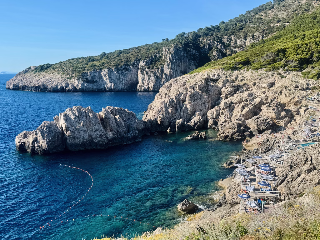 Rocky coastline with turquoise water and sunbeds near the lighthouse in Capri