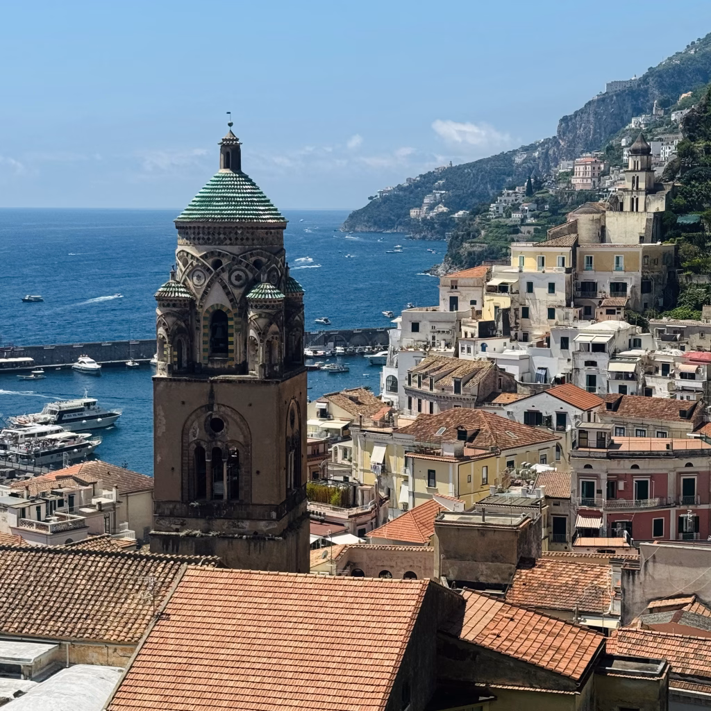 View over Amalfi’s rooftops, cathedral bell tower, and the blue sea with lush cliffs in the background