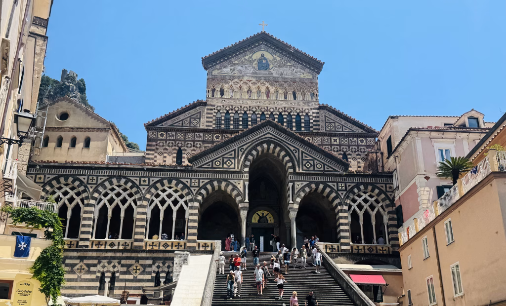 Striped façade and grand staircase of Amalfi Cathedral under a clear blue sky.