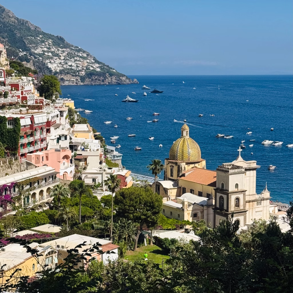 View of colorful hillside homes and the dome of Santa Maria Assunta overlooking the sea in the Amalfi town of Positano, Italy.