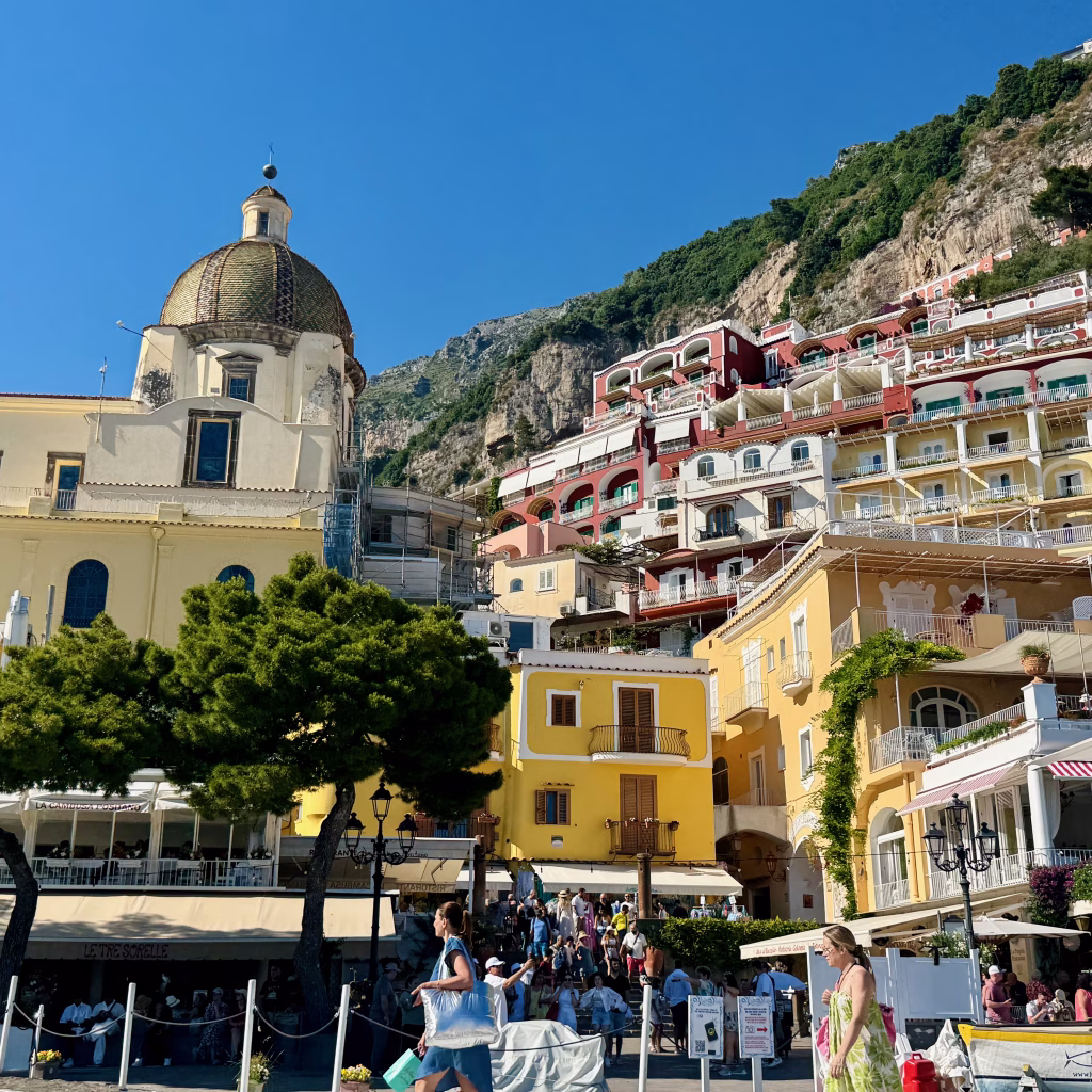 Dome of Santa Maria Assunta and colorful hillside buildings in Positano under a bright blue sky.
